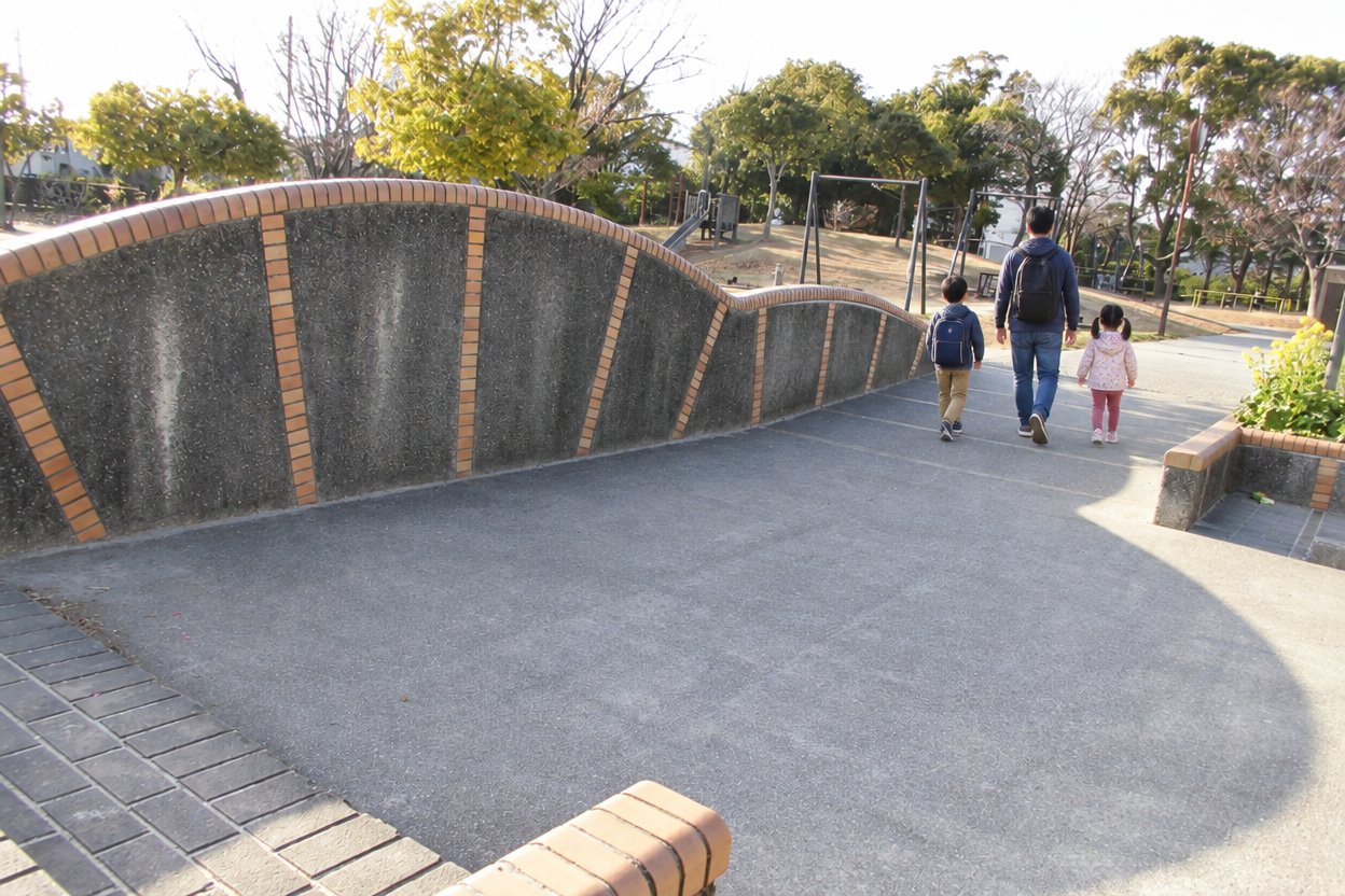笹原公園の入口から奥の遊具へ歩いていく父親と子ども2人の後ろ姿