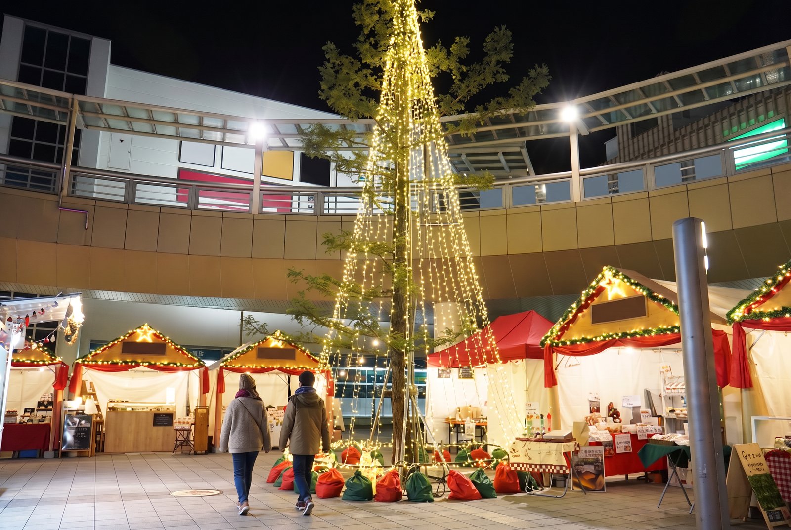 豊橋駅前のとよはしクリスマスマーケットで、光のツリーと屋台が並ぶ広場を歩く人の冬の夜景